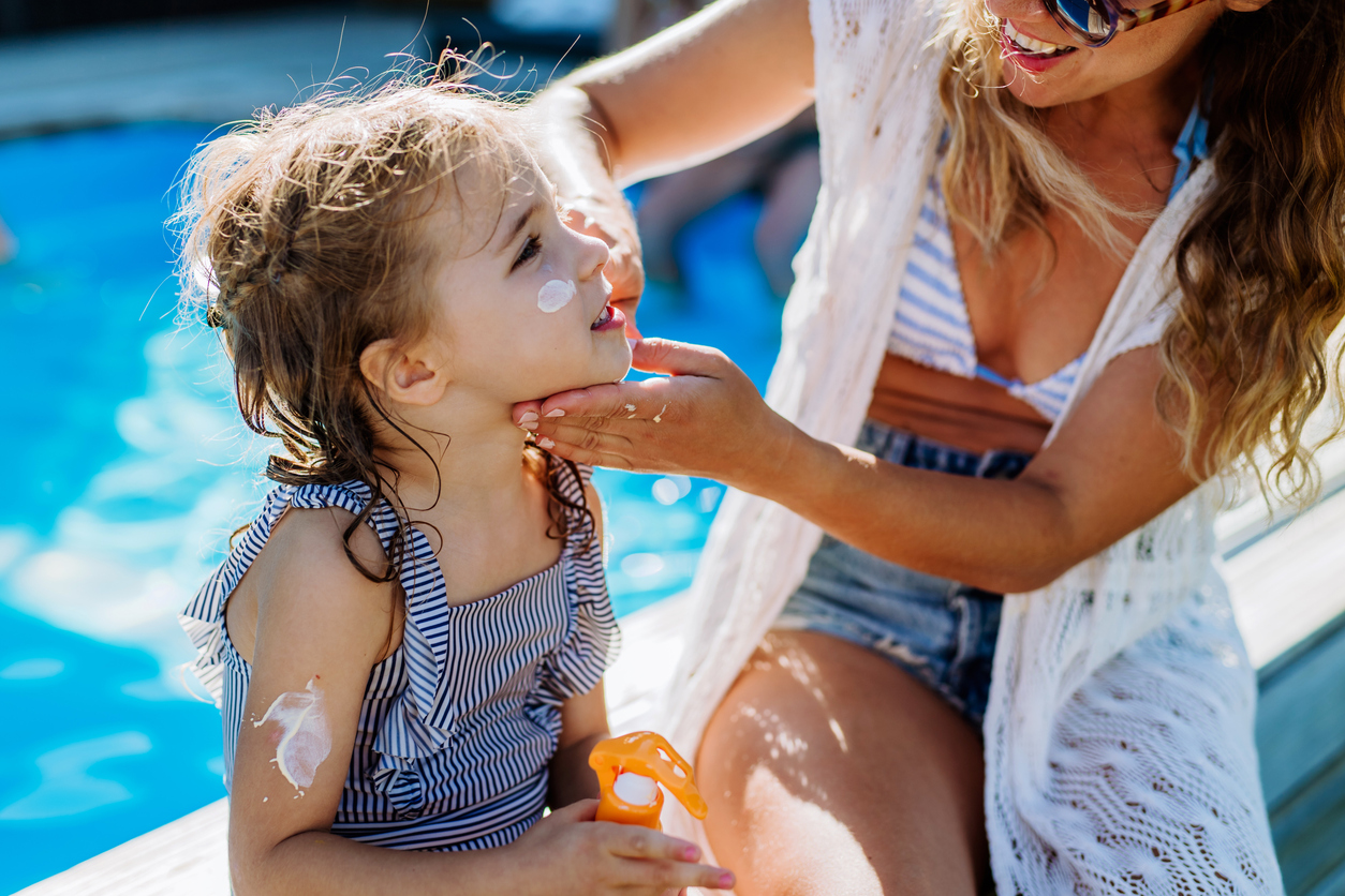 mother applying sunscreen to daughter's face at the pool